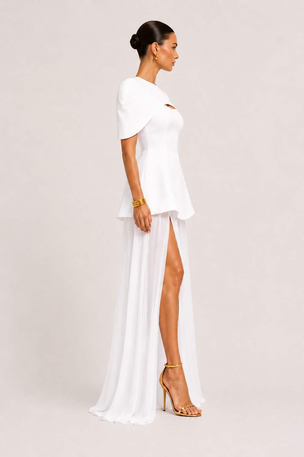Woman wearing a white dress with a high slit on a plain background
